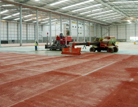 Applying Sika Chapdur dry-shake floor hardener to a fresh warehouse slab